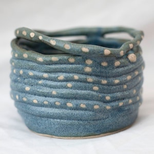 May include: A blue ceramic bowl with white dots and a raised rim. The bowl is handmade and has a rustic, organic feel.