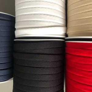 Peut inclure: Gros plan sur six bobines de galon élastique de différentes couleurs : blanc, beige, bleu marine, noir et rouge. Le galon est plié et empilé les uns sur les autres.