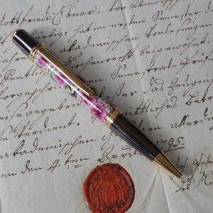 Könnte beinhalten: Ein schwarzer und goldener Stift mit einem floralen Design auf dem Schaft. Der Stift liegt auf einem Blatt Papier mit handschriftlichem Text. Der Text enthält das Datum "April 1795."