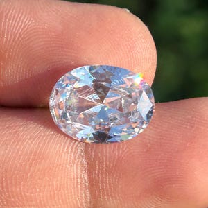 Puede incluir: Una gema ovalada transparente con un corte facetado, que muestra un arcoíris de colores cuando la luz brilla a través de ella.