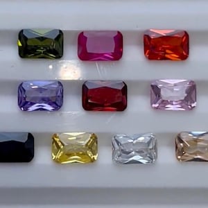 Könnte beinhalten: Sortiment aus zehn rechteckigen Edelsteinen in verschiedenen Farben, darunter Grün, Rot, Lila, Rosa, Schwarz, Gelb, Klar und Braun.