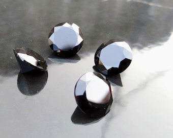 May include: Four black round gemstones with a faceted cut. The gemstones are on a gray surface.