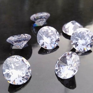 Puede incluir: Un grupo de siete cristales transparentes, redondos, facetados, en forma de diamante sobre una superficie negra.