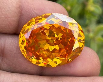 May include: A large, oval-shaped, faceted gemstone with a bright orange color. The gemstone is cut with many facets, giving it a sparkling appearance.