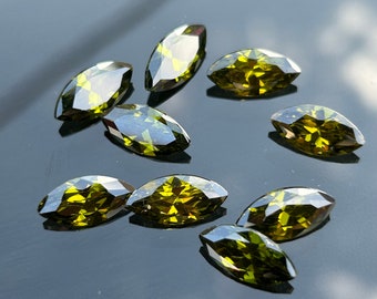 May include: A group of nine marquise-shaped green gemstones. The gemstones are faceted and have a shiny, reflective surface.