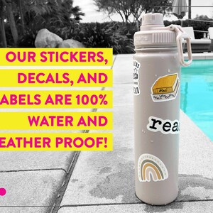 May include: A light brown water bottle with a black lid and a carrying handle. The bottle has several colorful stickers on it, including a rainbow, a book, and the word "read". The text "OUR STICKERS, DECALS, AND LABELS ARE 100% WATER AND WEATHER PROOF!" is displayed in yellow and pink on a white background.