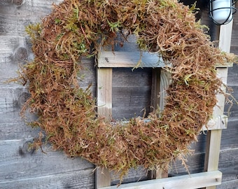 May include: A brown and green moss wreath hanging on a wooden fence. The wreath is made of natural materials and has a rustic look.