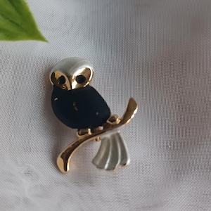 以下が含まれることがあります： 黒い体、銀色の羽、白と金の頭を持つ、金色のフクロウのブローチ。 フクロウは金の枝にとまっています。 ジャケット、スカーフ、バッグ用のユニークなアクセサリーです。