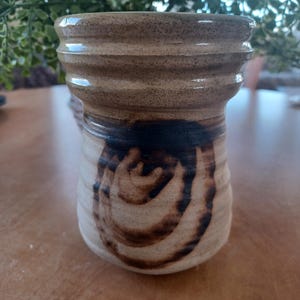 May include: A brown ceramic vase with a swirl design in a darker brown glaze. The vase has a wide mouth and a rounded body.