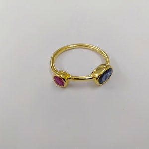 May include: Gold ring with a blue oval gemstone and a red round gemstone.