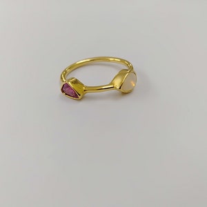 May include: A gold ring featuring a pink and white gemstone. The ring is simple and elegant.