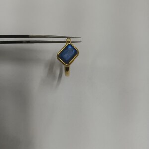May include: A gold ring with a blue gemstone set in a square shape.