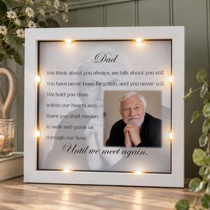 May include: A square white light-up shadow box frame featuring a memorial tribute to a father. The text reads: Dad, We think about you always, we talk about you still. You have never been forgotten, and you never will. We hold you close within our hearts and there you shall remain, to walk and guide us through our lives. Until we meet again. A color photograph of an older man is centered on the right side.