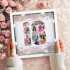 May include: A square white shadow box frame containing a personalized collage of photographs arranged in the shape of the number 18. The text reads Amelia, You have been loved for 18 years, and still counting, Happy 18th Birthday love always Nana.