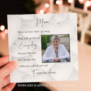 May include: A white card with a black border and a photo of an older woman. The card has the text "Mum" at the top and a poem about those we love don't go away, they walk beside us every day. The card is 15 cm by 15 cm.