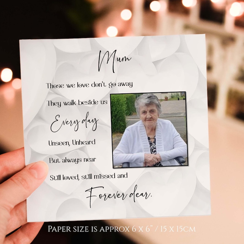 May include: A white card with a black border and a photo of an older woman. The card has the text "Mum" at the top and a poem about those we love don't go away, they walk beside us every day. The card is 15 cm by 15 cm.