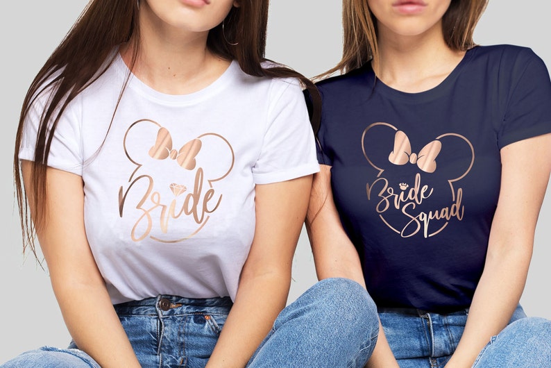 May include: Two white and navy blue t-shirts with a rose gold Mickey Mouse head design. The white shirt says "Bride" and the navy shirt says "Bride Squad".