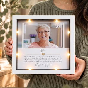 May include: A square white shadow box frame with integrated LED lights containing a photograph of an older person. Below the photo, the text reads: Mum, a gold heart icon, and a memorial poem ending with the phrase Until we meet again.