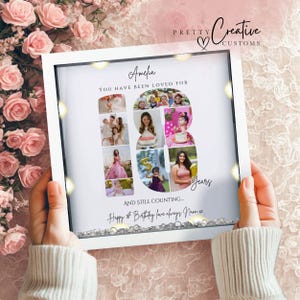 May include: A square white shadow box frame containing a photo collage arranged in the shape of the number 18. The text reads Amelia, YOU HAVE BEEN LOVED FOR 18 Years, AND STILL COUNTING... Happy 18th Birthday love always Nann xx. Clear crystals fill the base.