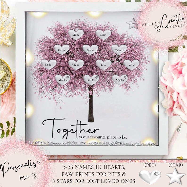 Op de afbeelding: Een wit ingelijst verlicht beeld met een roze kersenbloesemboom met harten aan de takken. Elk hart heeft een naam erop geschreven. De tekst "Together is our favourite place to be." staat onder de boom. De tekst "Personalise me" staat linksonder. De tekst "2-25 NAMES IN HEARTS, PAW PRINTS FOR PETS & 3 STARS FOR LOST LOVED ONES" staat onderin het midden. Een zilveren pootprint en een zilveren ster zijn rechtsonder afgebeeld.