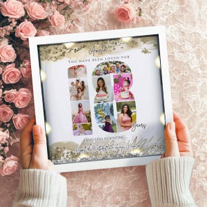 May include: A square white shadow box frame containing a photo collage shaped like the number 18. The text reads Amelia, You have been loved for 18 years, and still counting... Happy 18th Birthday love always Nann xx. Gold glitter accents decorate the top and bottom.