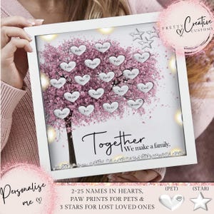 May include: A white frame with a pink tree and silver hearts. The hearts have names written on them. The text "Together We make a family." is at the bottom of the frame. The frame has a light behind it. The text "2-25 NAMES IN HEARTS, PAW PRINTS FOR PETS & 3 STARS FOR LOST LOVED ONES" is below the frame. There is a silver paw print and a silver star below the text.