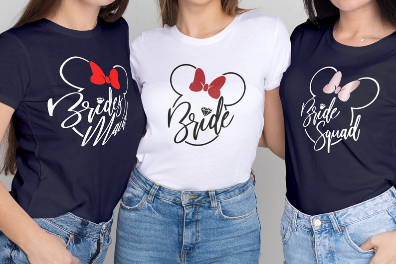 May include: Three navy blue t-shirts with white text and a white outline of Mickey Mouse ears with a red bow. The text on the shirts reads "Bride", "Bridesmaid", and "Bride Squad".
