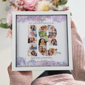 May include: A square white shadow box frame containing a personalized photo collage arranged in the shape of the number 18. The design features purple watercolor accents, the text Amelia, YOU HAVE BEEN LOVED FOR, Years, AND STILL COUNTING.