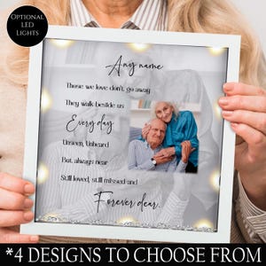 May include: White picture frame with a black and white photo of an older couple. The frame has a white background with the text "Those we love don't go away. They walk beside us Every day Unseen, Unheard But always near Still loved, still missed and Forever dear." The frame has optional LED lights.
