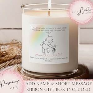 May include: A large white candle in a clear glass jar. The candle features a label with a Winnie the Pooh illustration and text. The text includes a quote and a personalized message. The candle sits on a decorative coaster.