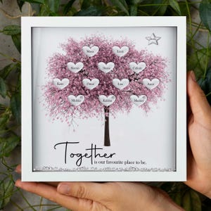 Op de afbeelding: Een wit ingelijst beeld met een roze kersenbloesemboom met zilveren harten op de takken. Elk hart heeft een naam erop geschreven. De tekst "Together is our favourite place to be." staat onderaan het beeld.