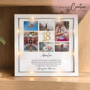 May include: A white square shadow box frame with integrated LED lights containing a photo collage of five images, a gold number 18, and the name Amelia. The text reads: EIGHTEEN YEARS, WHAT A WONDERFUL AGE, A BRAND-NEW CHAPTER, A BRAND-NEW PAGE.