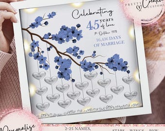 Puede incluir: Un marco blanco con un diseño floral azul y plateado. El marco tiene un mensaje personalizado que dice "Celebrando 45 años de amor" y "16,436 días de matrimonio". El marco también tiene una lista de nombres y símbolos para mascotas y seres queridos.