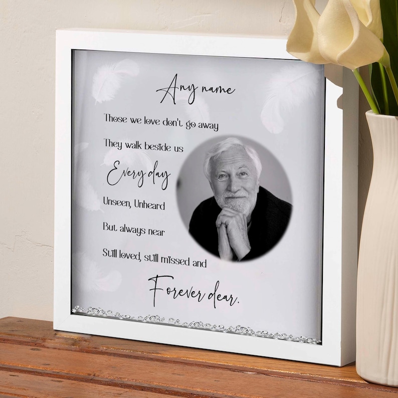 May include: White framed memorial box with a black and white photo of a man and a poem that reads "Those we love don't go away, They walk beside us Every day, Unseen, Unheard, But always near, Still loved, still missed and Forever dear."