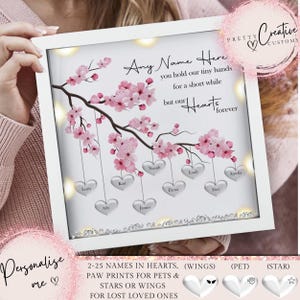 May include: White framed light-up memorial with a pink cherry blossom branch and silver hearts hanging from it. The hearts have names written on them. The text reads "Any Name Here you hold our tiny hands for a short while but our Hearts forever".