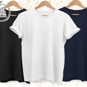 May include: Three blank t-shirts, one black, one white, and one navy blue, hanging on wooden hangers. The shirts are all plain and have no designs or text.