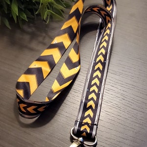 May include: A black and gold lanyard with a chevron pattern and a silver clip.