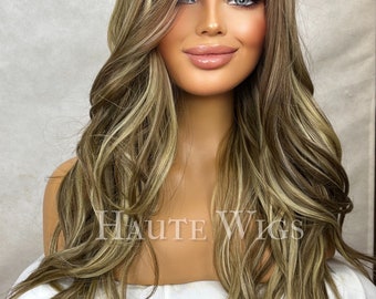 Op de afbeelding: Een lange, golvende pruik met blonde en bruine highlights. De pruik heeft een kanten voorkant en is gestyled met losse krullen. De tekst "HAUTE WIGS" is zichtbaar op de voorkant van de pruik.
