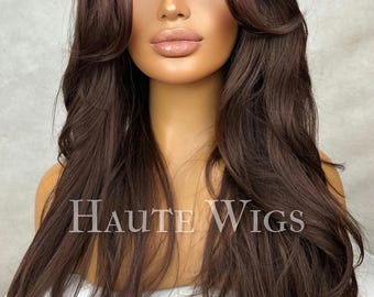 May include: A long, brown, wavy synthetic wig with a lace front. The wig is styled with a side part and layers. The wig is on a mannequin head.