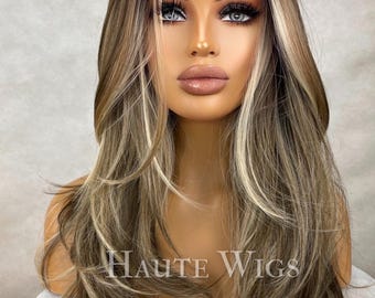Könnte beinhalten: Lange, wellige, hellbraune Perücke mit blonden Strähnen. Die Perücke ist in einem geschichteten, zerzausten Look gestylt. Die Perücke befindet sich auf einem Mannequin-Kopf. Der Text "HAUTE WIGS" ist am unteren Rand des Bildes sichtbar.