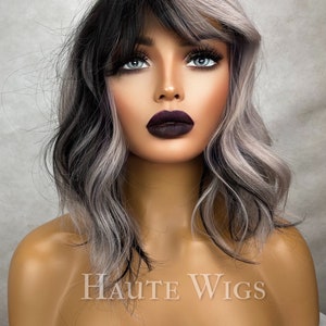 May include: A black and silver wig with a side part and bangs. The wig is styled in loose waves. The wig is on a mannequin head.