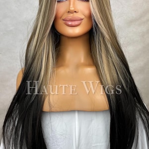 Könnte beinhalten: Eine lange, mehrschichtige Perücke mit einer Mischung aus Blond-, Schwarz- und Brauntönen. Die Perücke hat einen dunklen Ansatz, geht in blonde Highlights über und endet mit schwarzen Spitzen. Der Text "Haute Wigs" ist sichtbar.