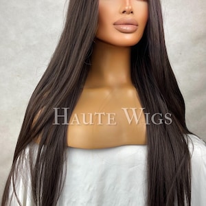 Peut inclure: Tête de mannequin avec une longue perruque brun foncé aux mèches raides et lisses. La perruque présente une implantation naturelle et une raie au milieu. Le texte "HAUTE WIGS" est visible.