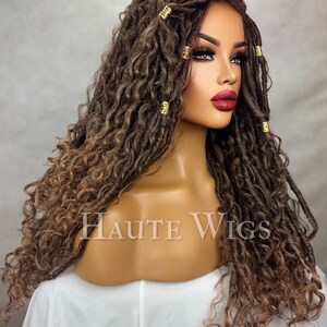 May include: A brown and blonde wig with long, curly dreadlocks. The wig features gold-colored hair accessories and is styled on a mannequin head. The text "HAUTE WIGS" is visible on the mannequin.
