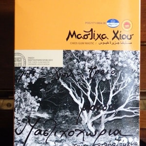 May include: A yellow box with a black and white photo of a tree with the text "Mastiha Chiou" and "Chios Gum Mastic" in black. The box is labeled with "500g" and "17.65 oz e".