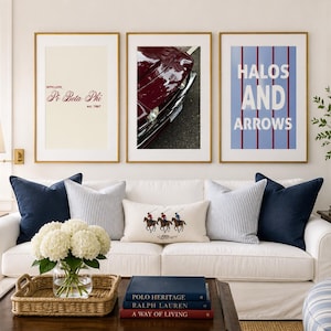 May include: A white sofa with navy blue and striped throw pillows, featuring a central lumbar pillow with a polo player graphic. Above the sofa are three framed prints: one with Pi Beta Phi text, one showing a maroon car, and one with Halos and Arrows text.