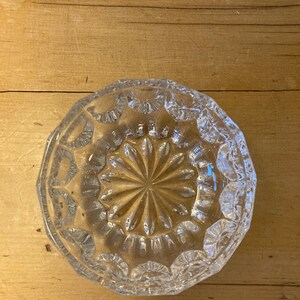 May include: A clear glass bowl with a decorative, starburst pattern. The bowl has a scalloped edge and is made of cut glass.