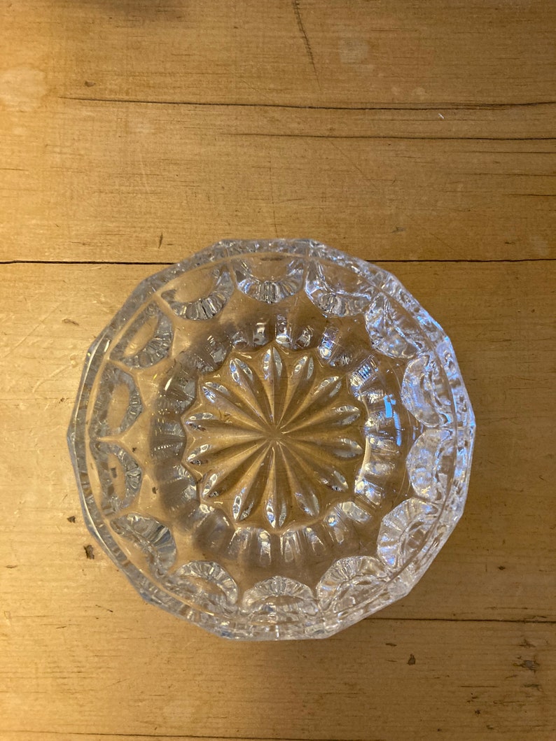 May include: A clear glass bowl with a decorative, starburst pattern. The bowl has a scalloped edge and is made of cut glass.