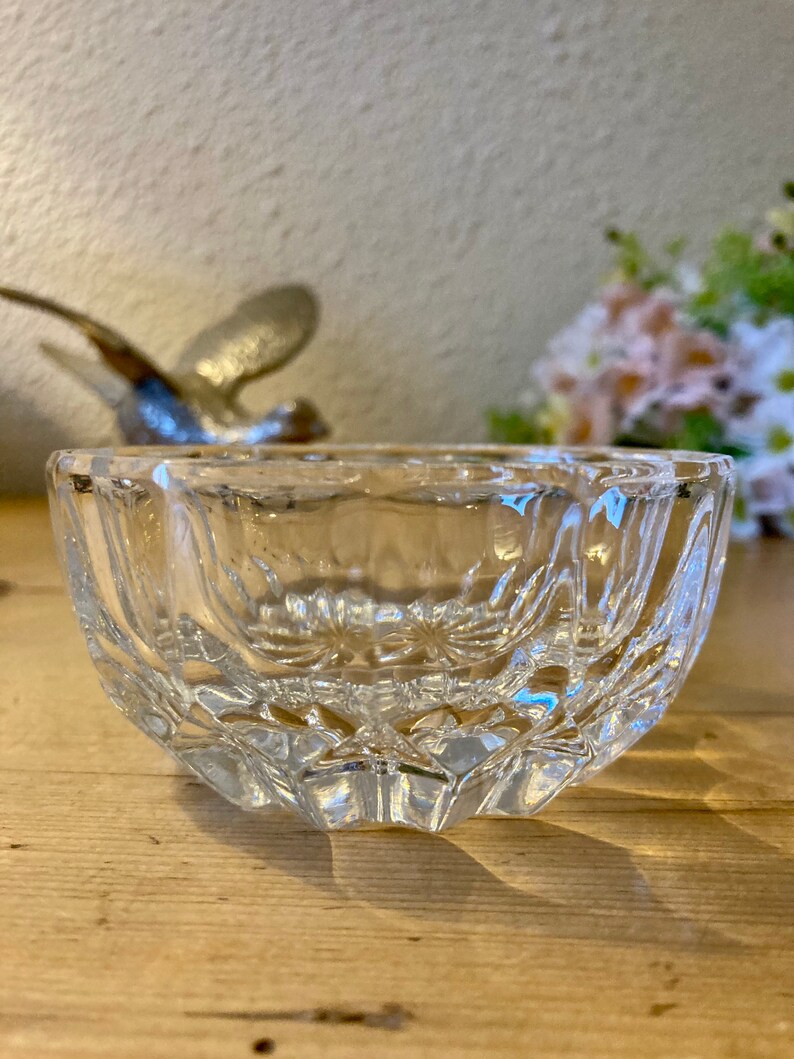 May include: A clear glass bowl with a cut-glass design. The bowl is sitting on a wooden surface.