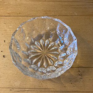 May include: A clear glass bowl with a cut-glass design. The bowl has a starburst pattern in the center and a scalloped edge.